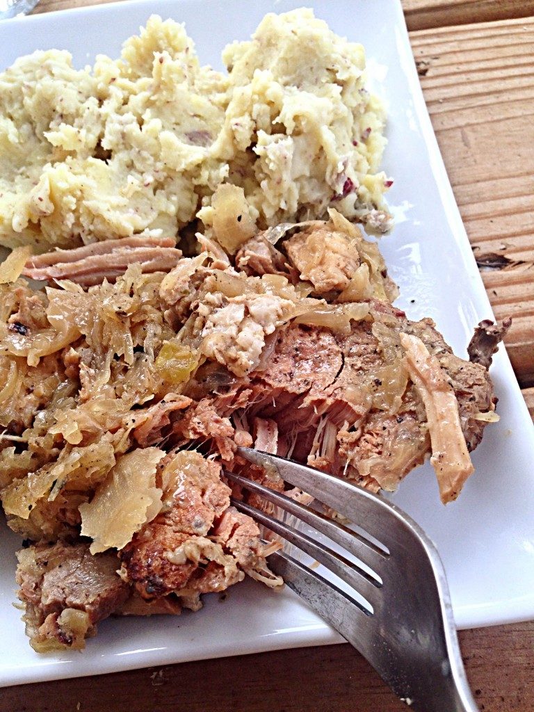 fork cutting into slow cooker pork chops with bacon and sauerkraut