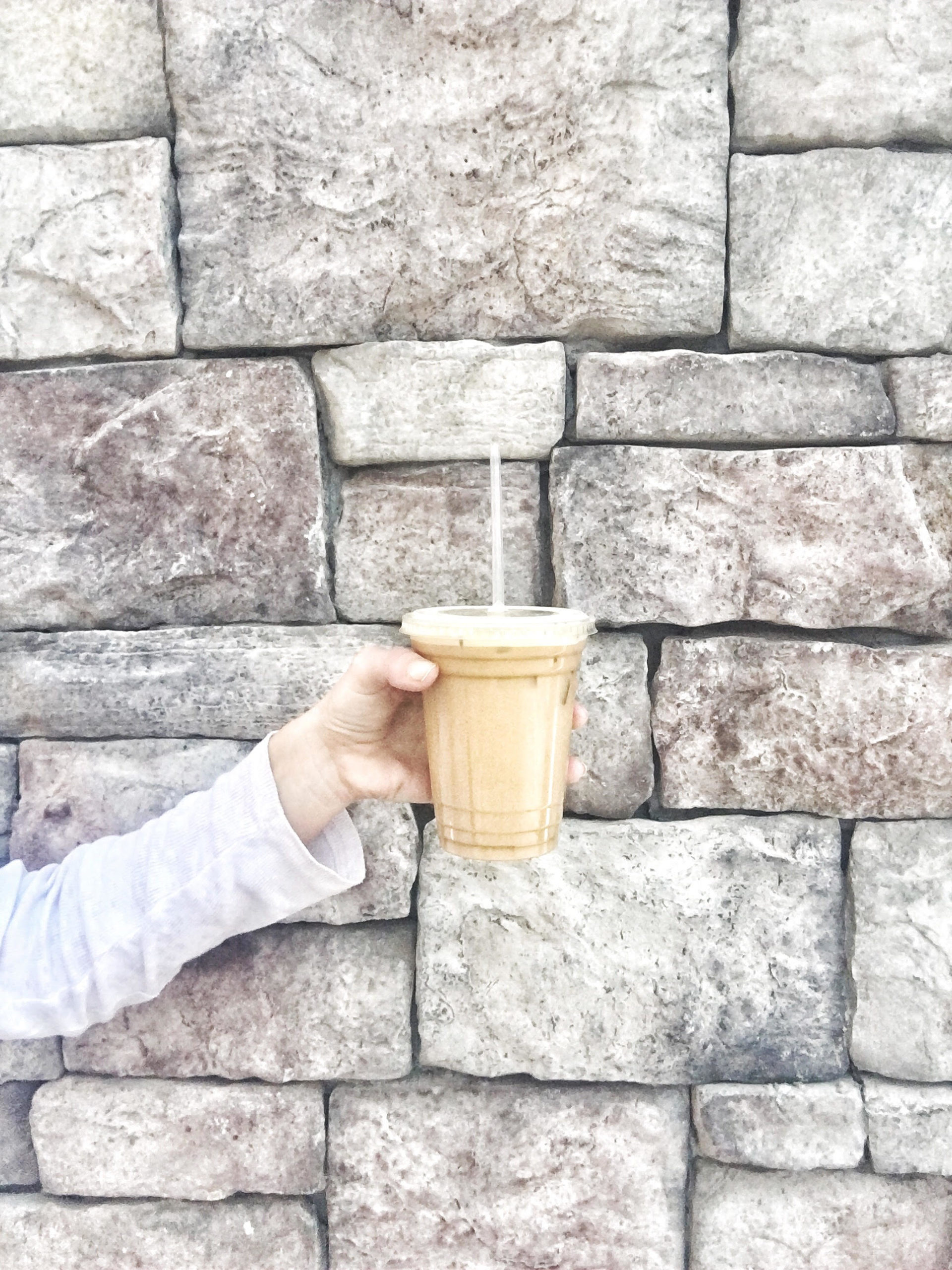 megan holding iced coffee with heavy cream against stone wall