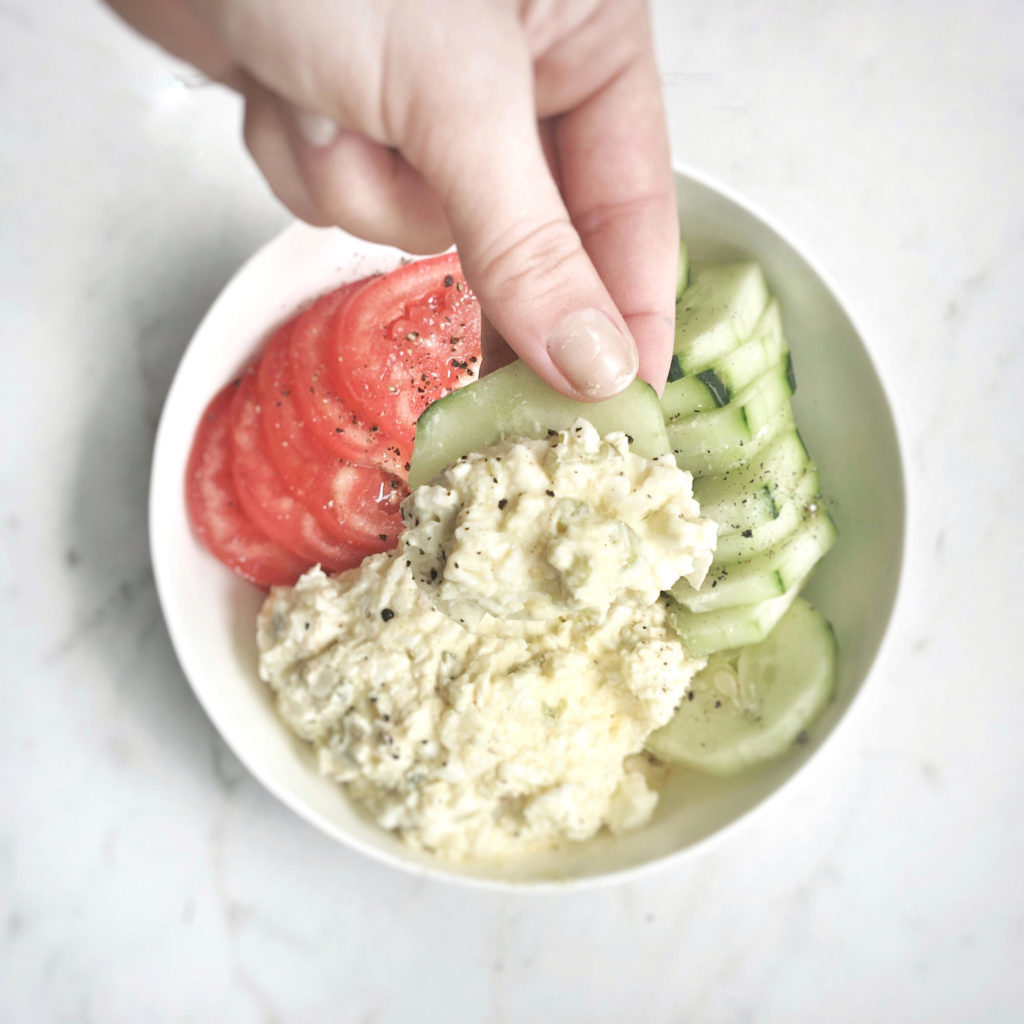 hand scooping egg salad with cucumber