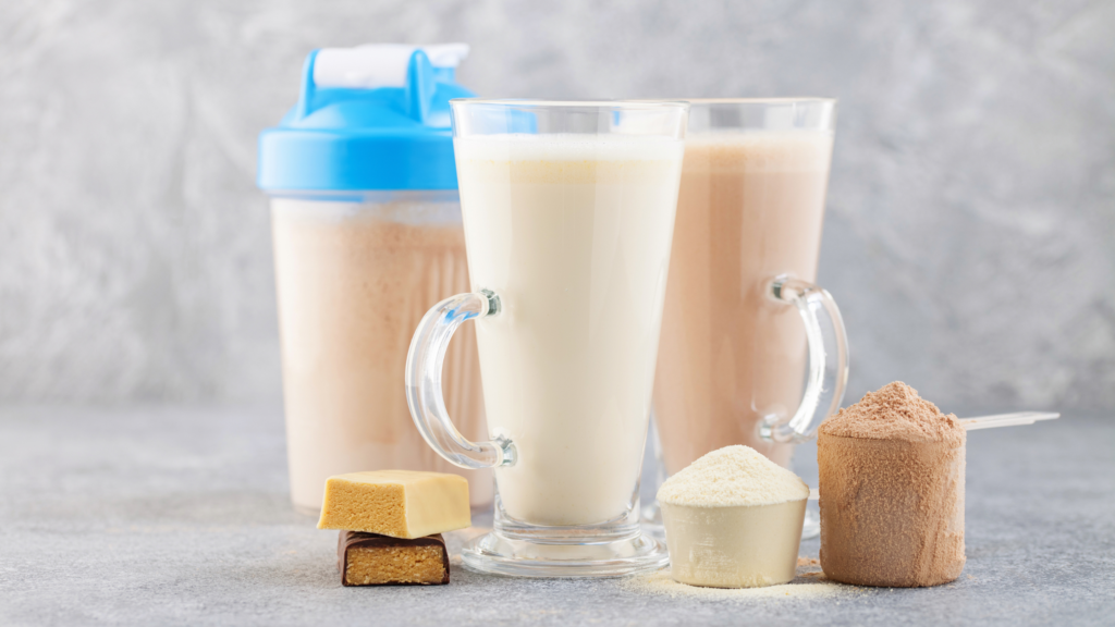 protein powder scoops, protein bar, chocolate and vanilla protein shakes in glass cups, and protein shake in shaker bottle