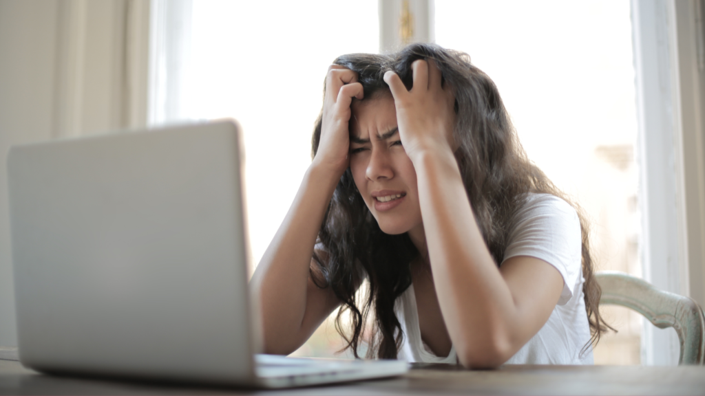 stressed-looking brunette woman staring at her laptop with her hands in her hair