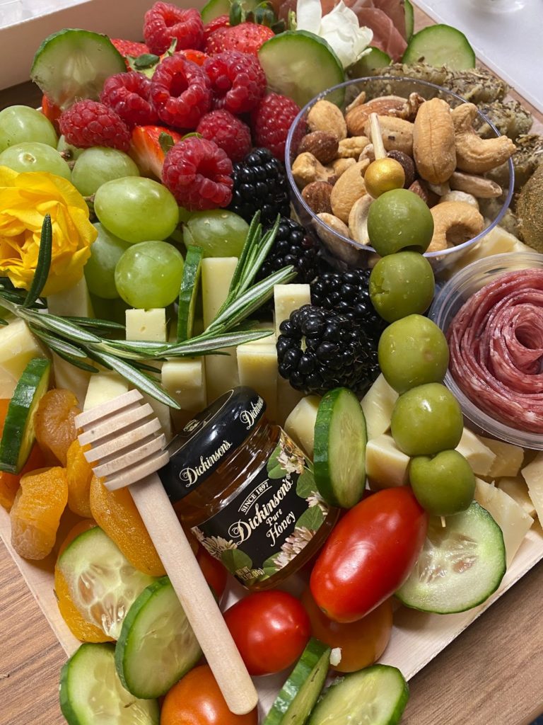 Baylee's charcuterie board: honey, honey stick, cucumbers, tomatoes, green olives, dried fruit, cheese, berries, grapes, mixed nuts